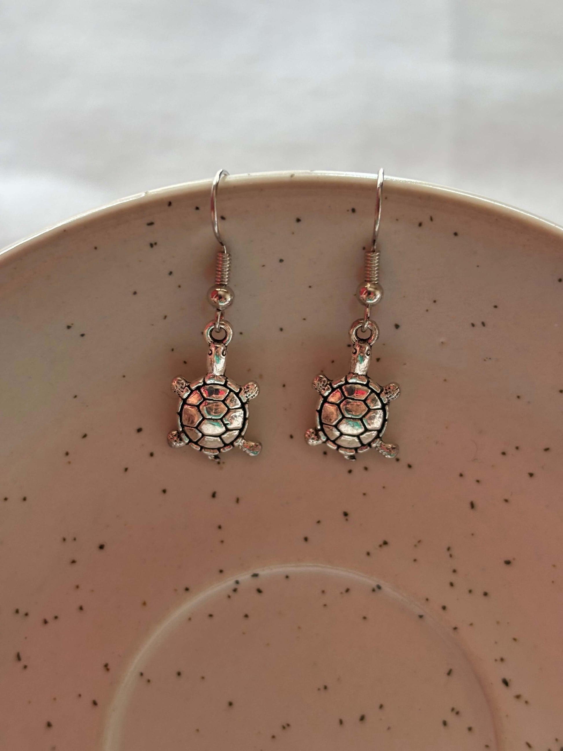 Elegant brass tortoise earrings on a speckled ceramic plate