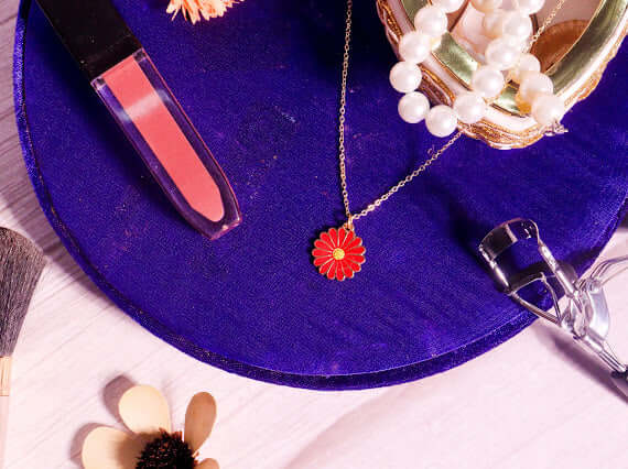 Red Daisy Necklace in stainless steel on a purple surface with makeup and accessories